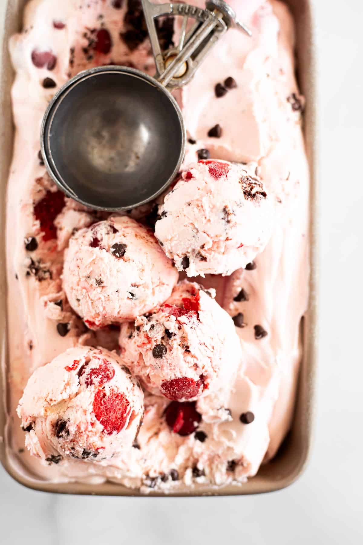4 scoops of no churn chocolate cherry ice cream in a loaf pan with an ice cream scoop.