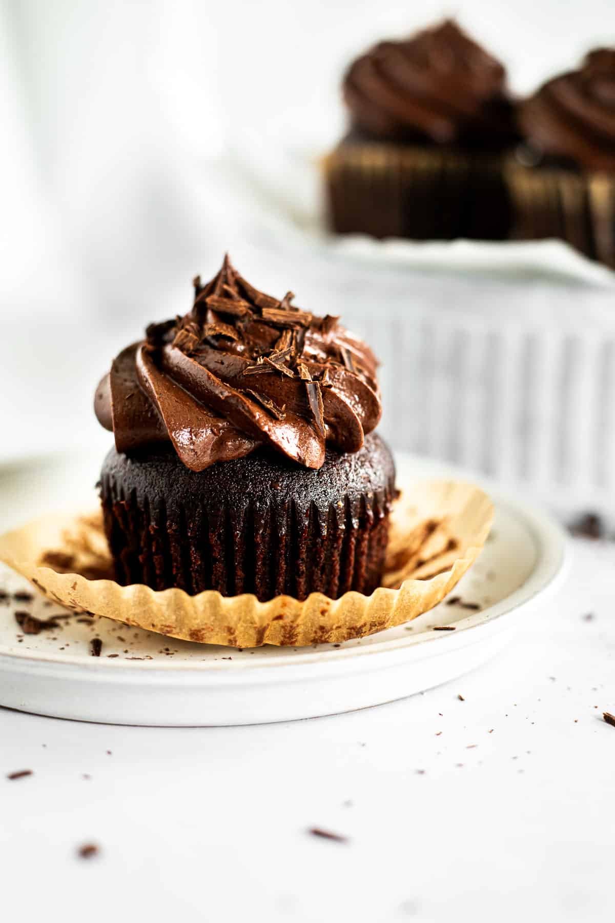 chocolate fudge cupcake with paper liner on a white plate.
