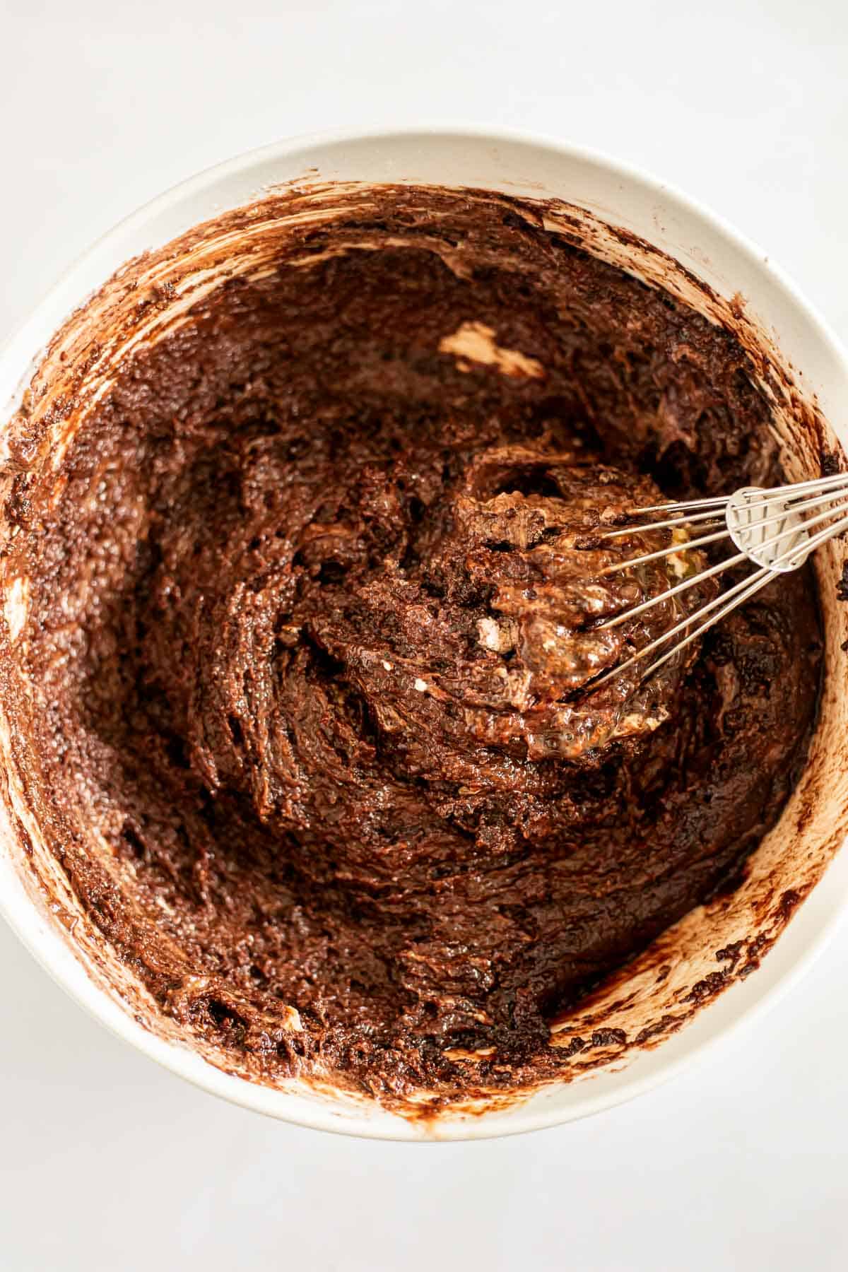 flour, sugar, and cocoa powder whisked with eggs and oil in a white bowl.