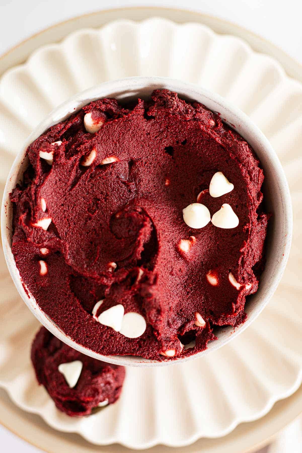 edible red velvet cookie dough with white chocolate chips in a white bowl.