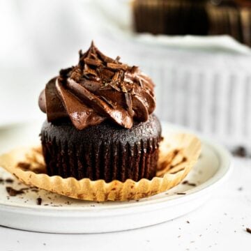 chocolate fudge cupcake with paper liner on a white plate.