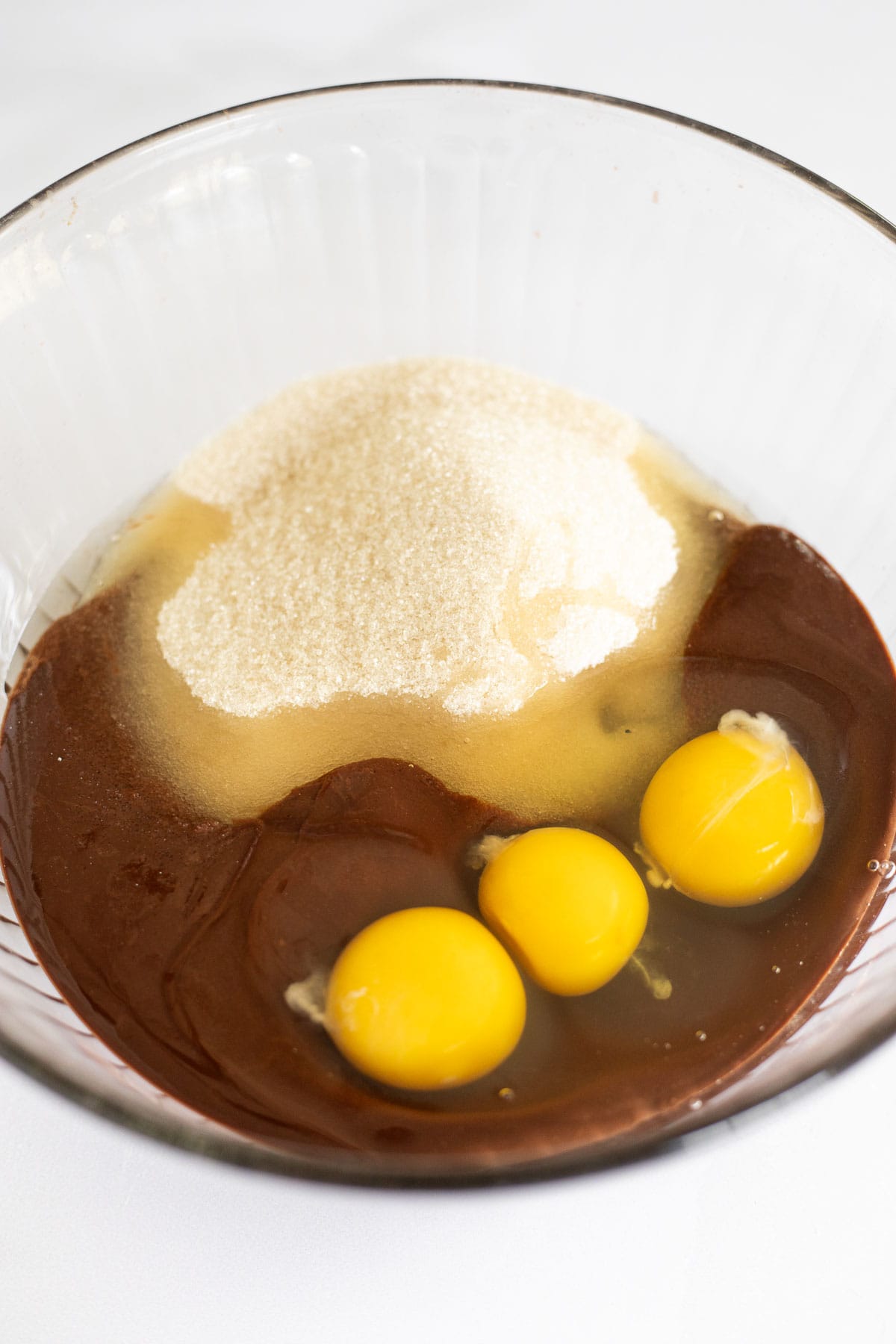 three eggs and sugar in a glass bowl of melted chocolate.