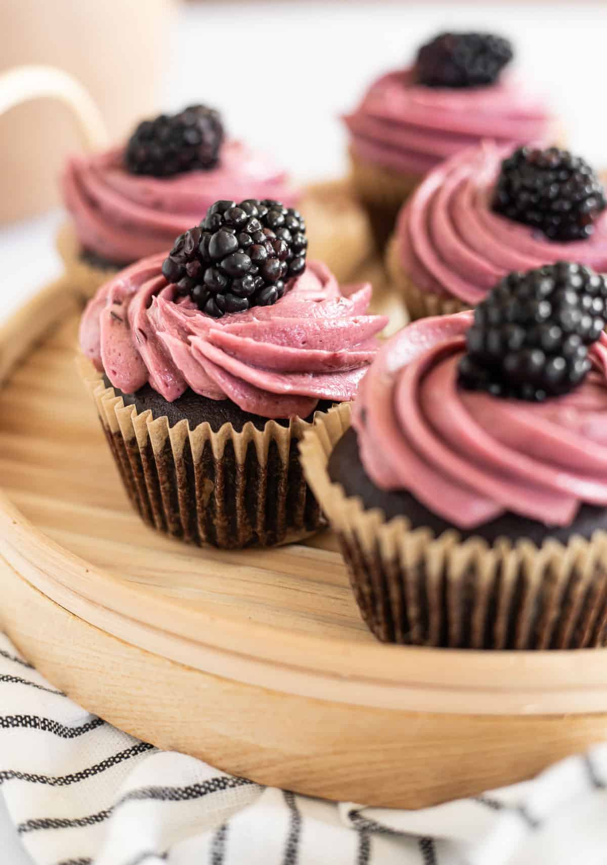 chocolate blackberry cupcakes on a wooden platter topped with fresh blackberries.