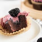 a chocolate cupcake with blackberries on a plate with a bite taken out of it.