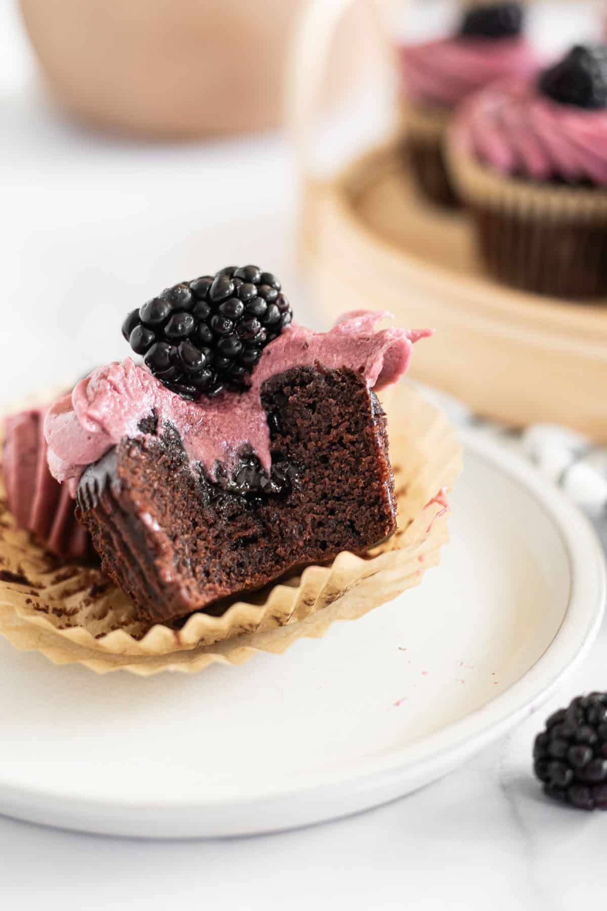 a chocolate cupcake with blackberries on a plate with a bite taken out of it.