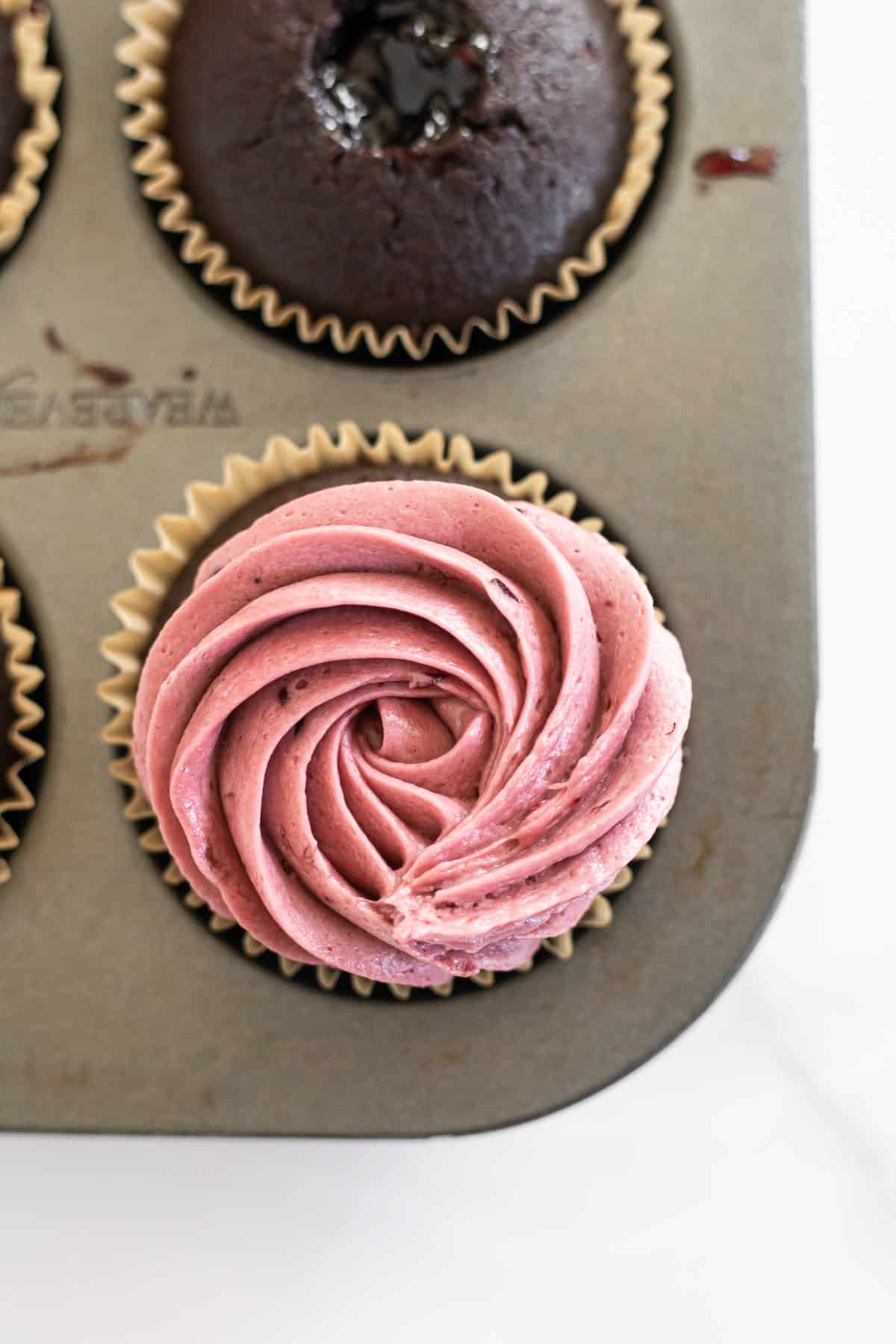 chocolate cupcake in a muffin pan topped with blackberry buttercream.