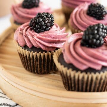 chocolate blackberry cupcakes on a wooden platter topped with fresh blackberries.