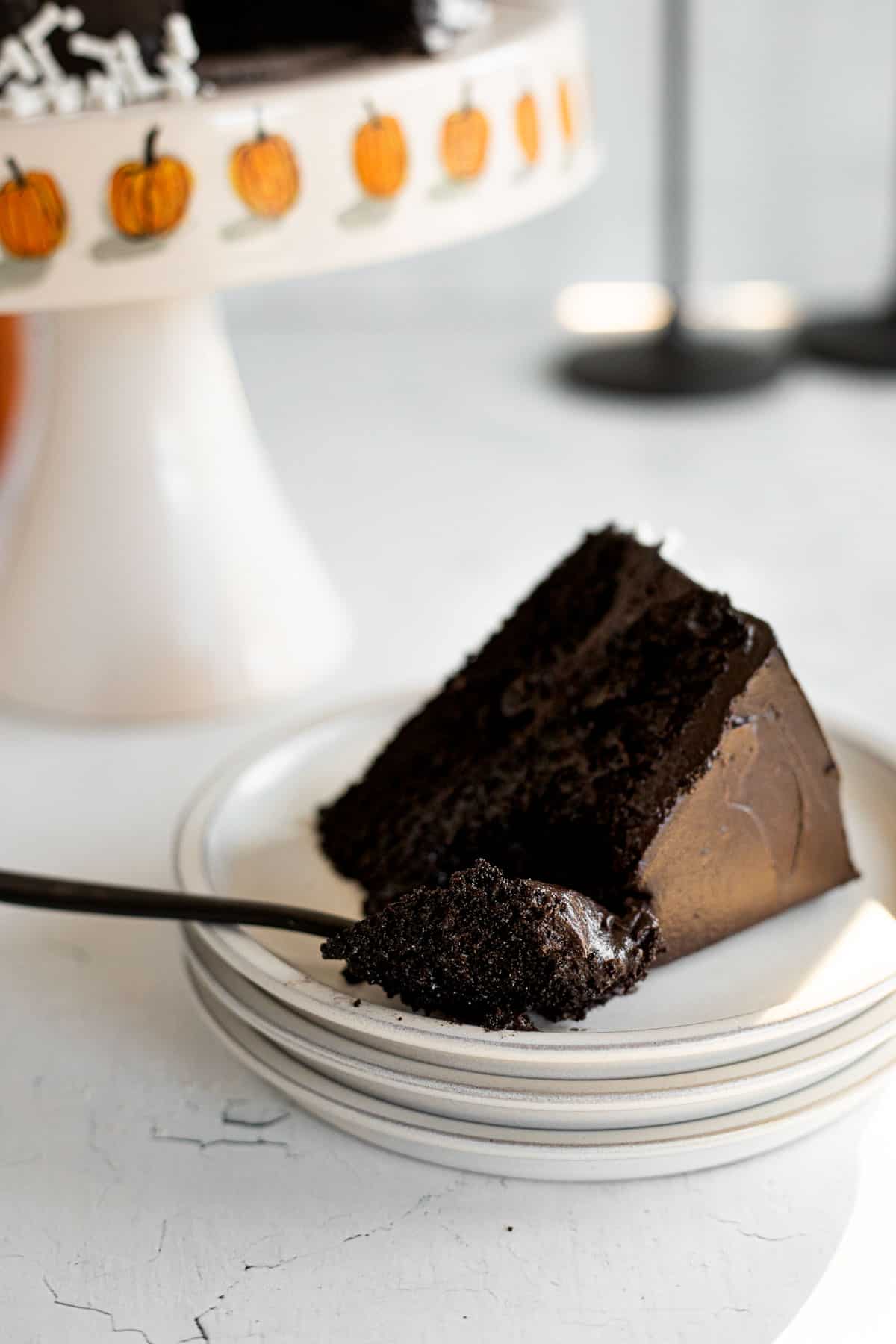 a slice of black cocoa cake on a white plate in front of a cake stand.