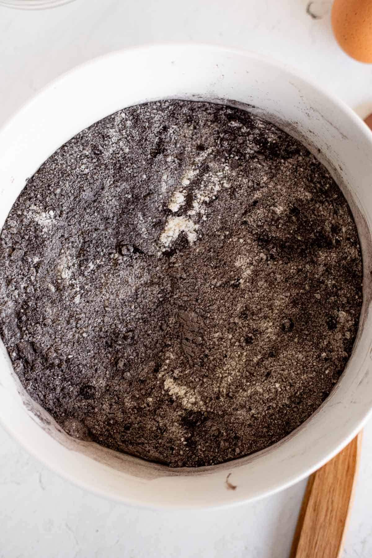 flour, sugar, and black cocoa powder whisked in a white mixing bowl.