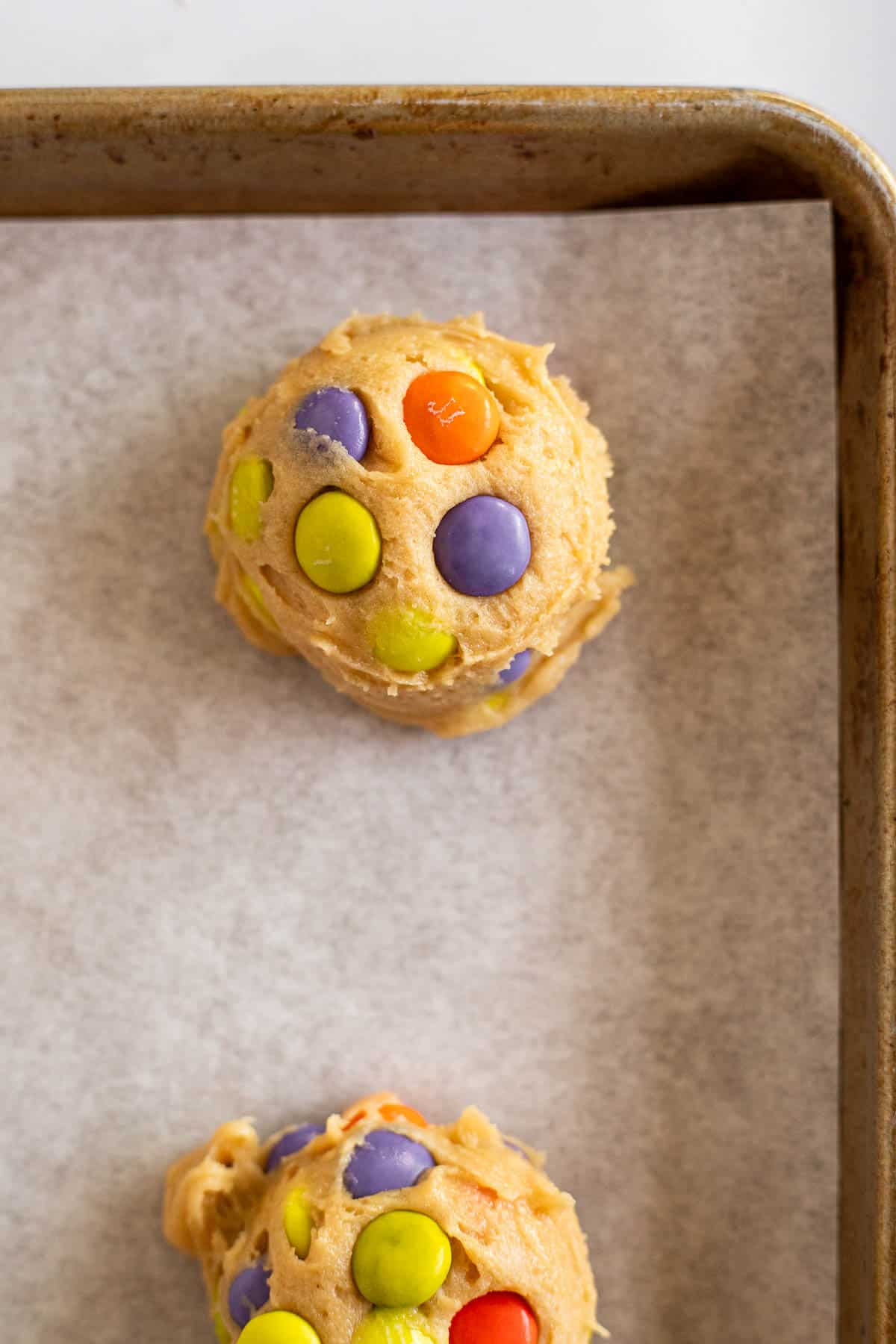 balls of M&M cookie dough on parchment lined baking sheet.