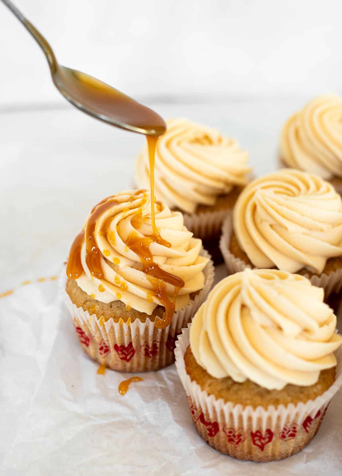 vanilla cupcake with frosting and caramel being drizzled on top.