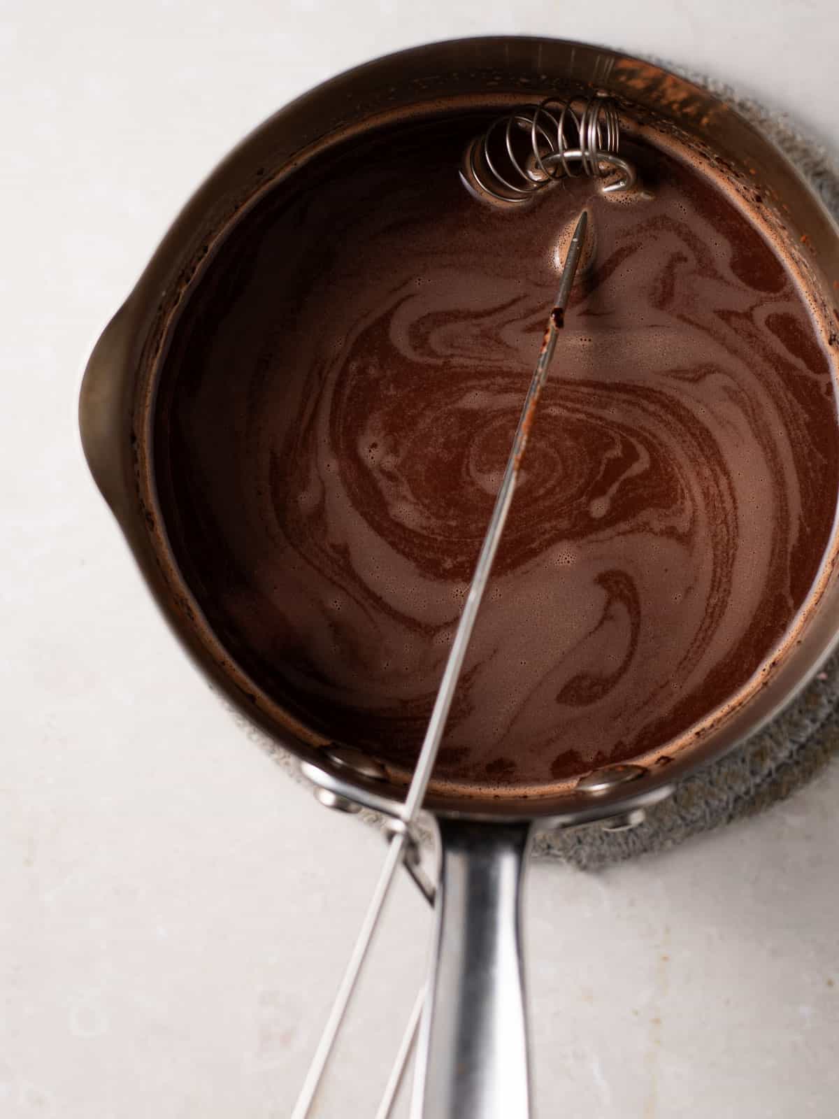 overhead photo of hot chocolate with bone broth in a pot with a whisk.