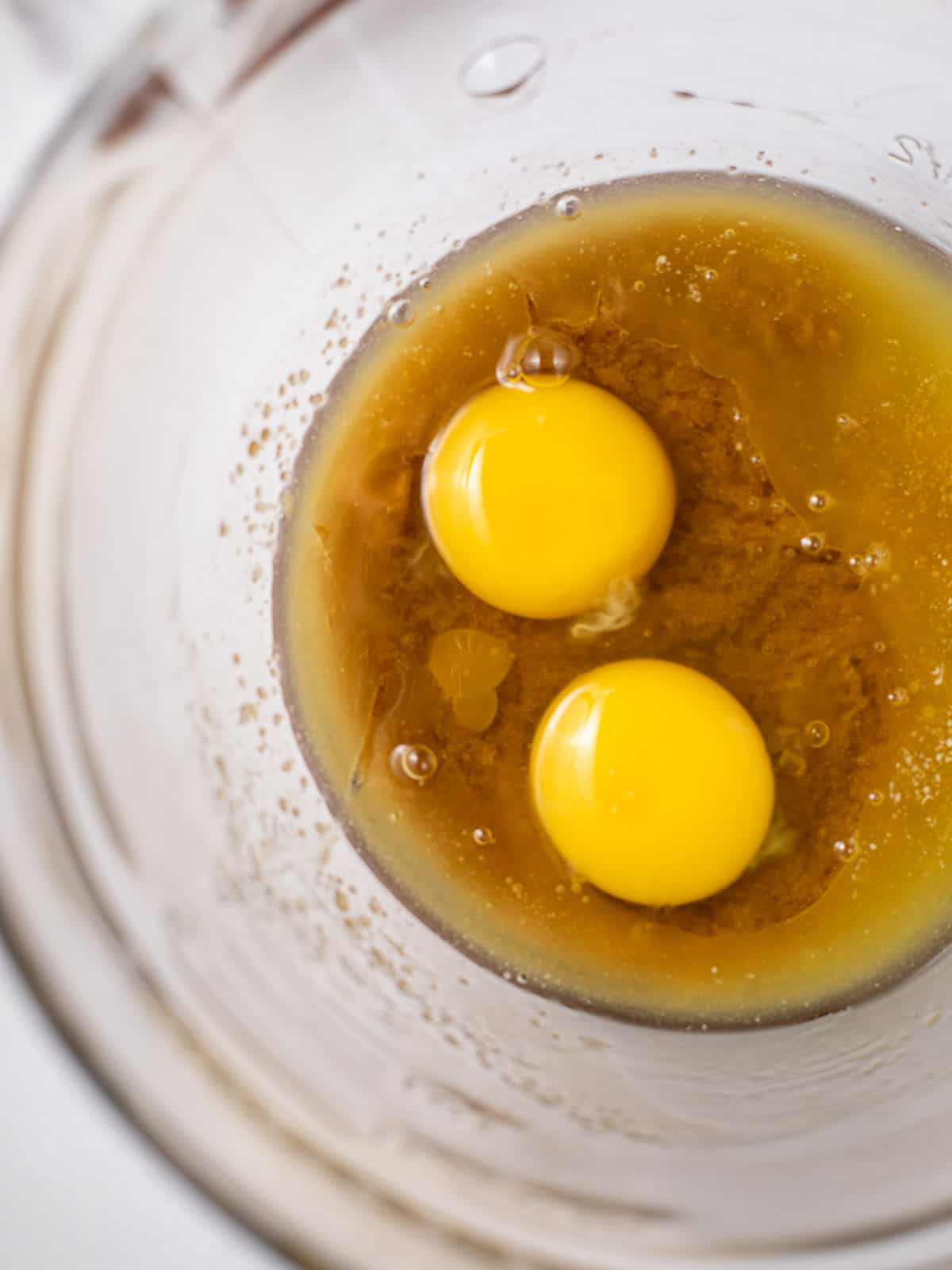 two cracked eggs in a glass bowl of melted butter and brown sugar.