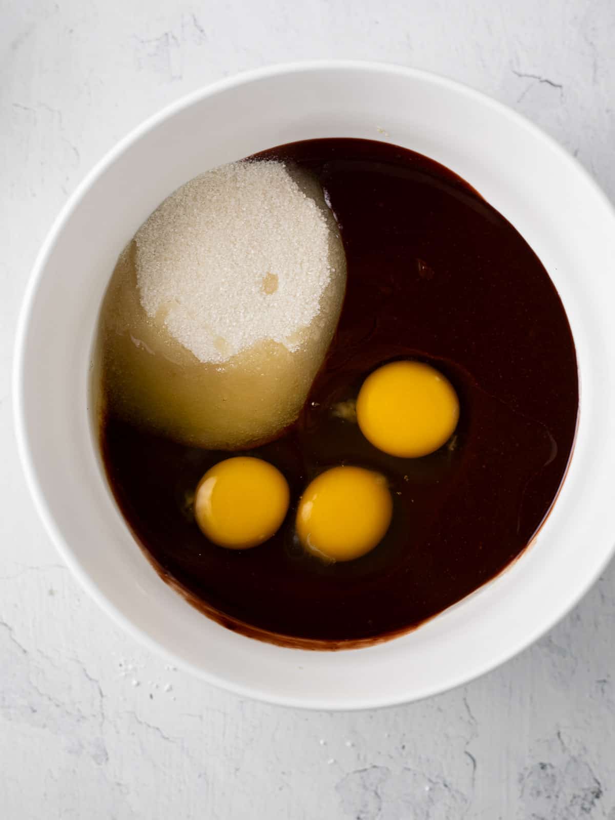 sugar and 3 eggs in a white bowl with melted chocolate.