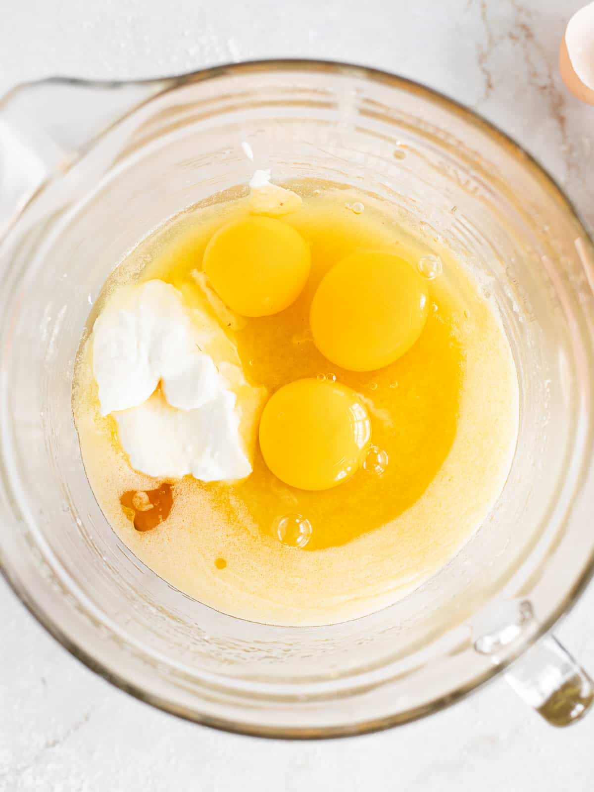 melted butter, sugar, eggs, and sour cream mixed together in a glass bowl.
