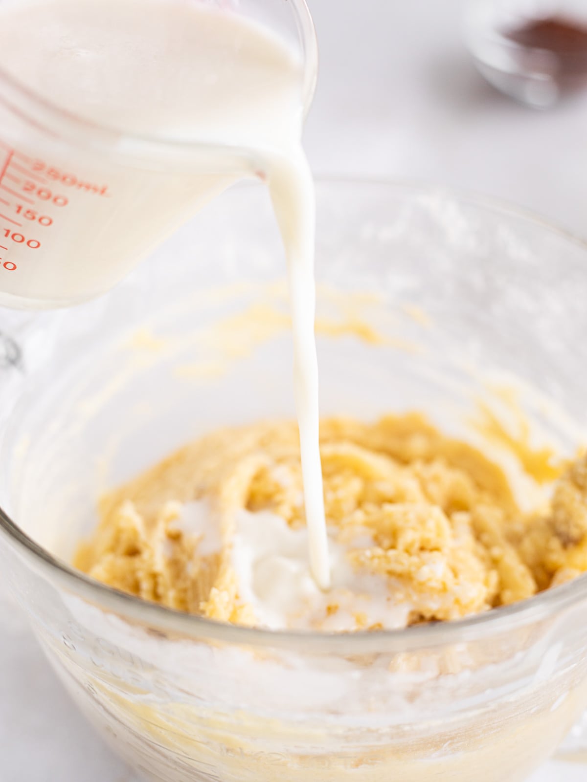 buttermilk pouring into a glass bowl of vanilla cake batter.