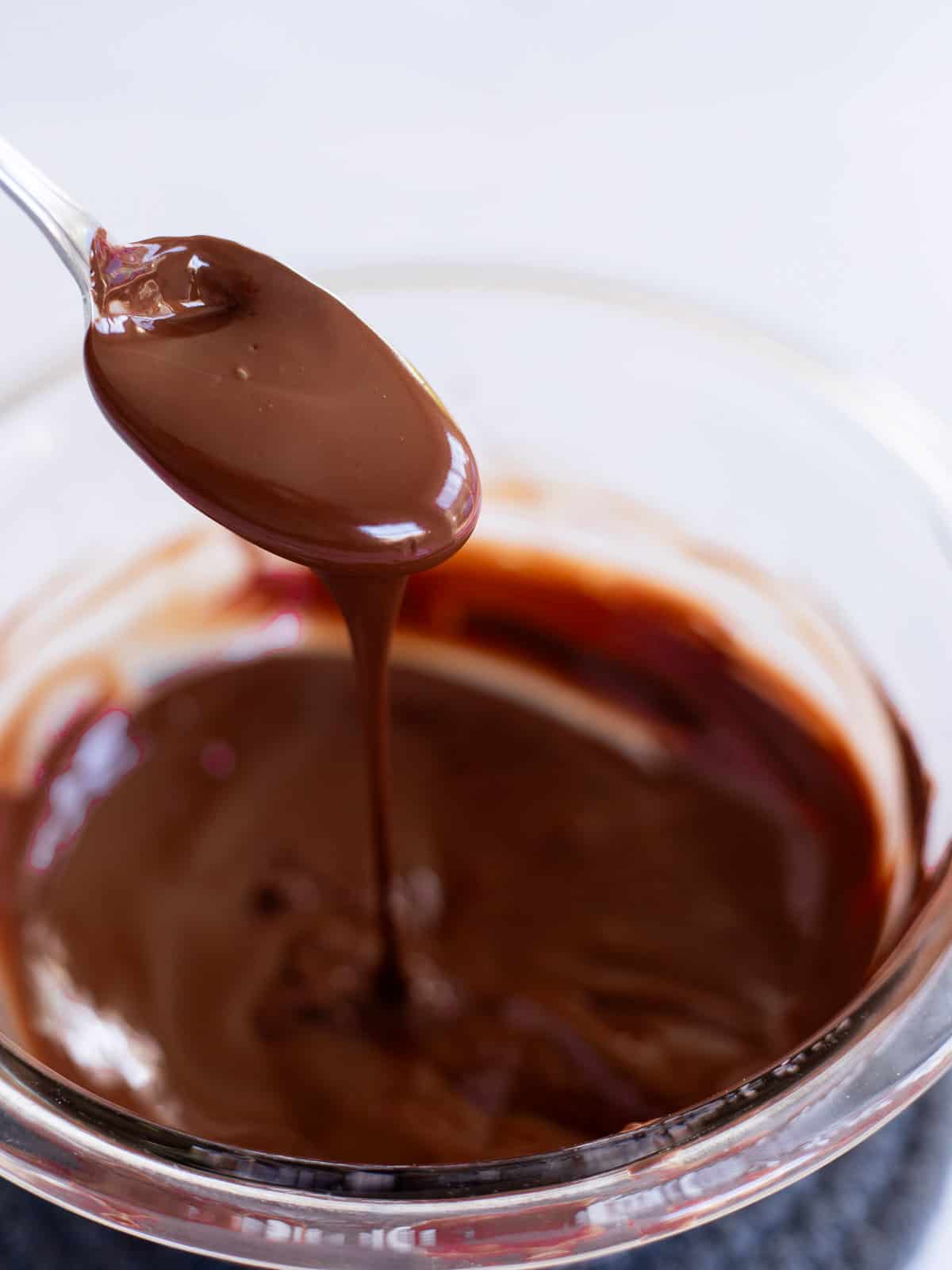 melted chocolate in a glass bowl dripping off a spoon.