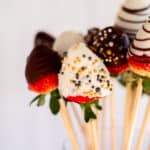 close up photo of chocolate covered strawberries on a stick in a vase.