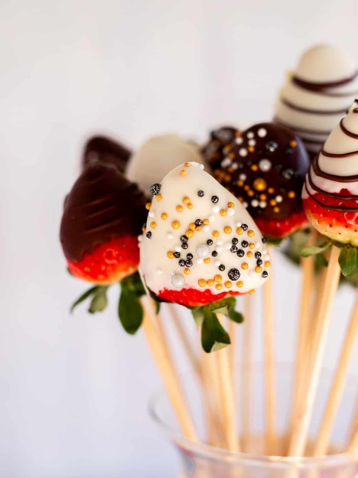 close up photo of chocolate covered strawberries on a stick in a vase.