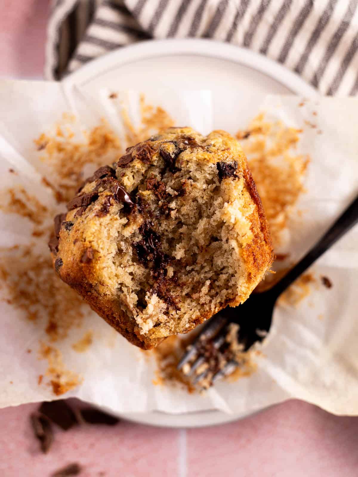 Bakery Style Banana Chocolate Chip Muffin on a white plate with a bite taken out of it.