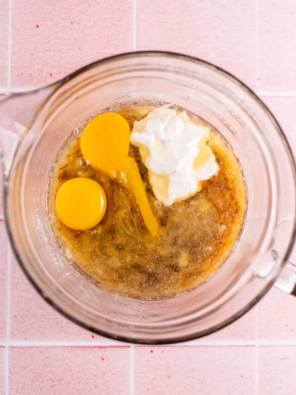 2 eggs, sour cream, and vanilla in a glass bowl with mashed bananas.