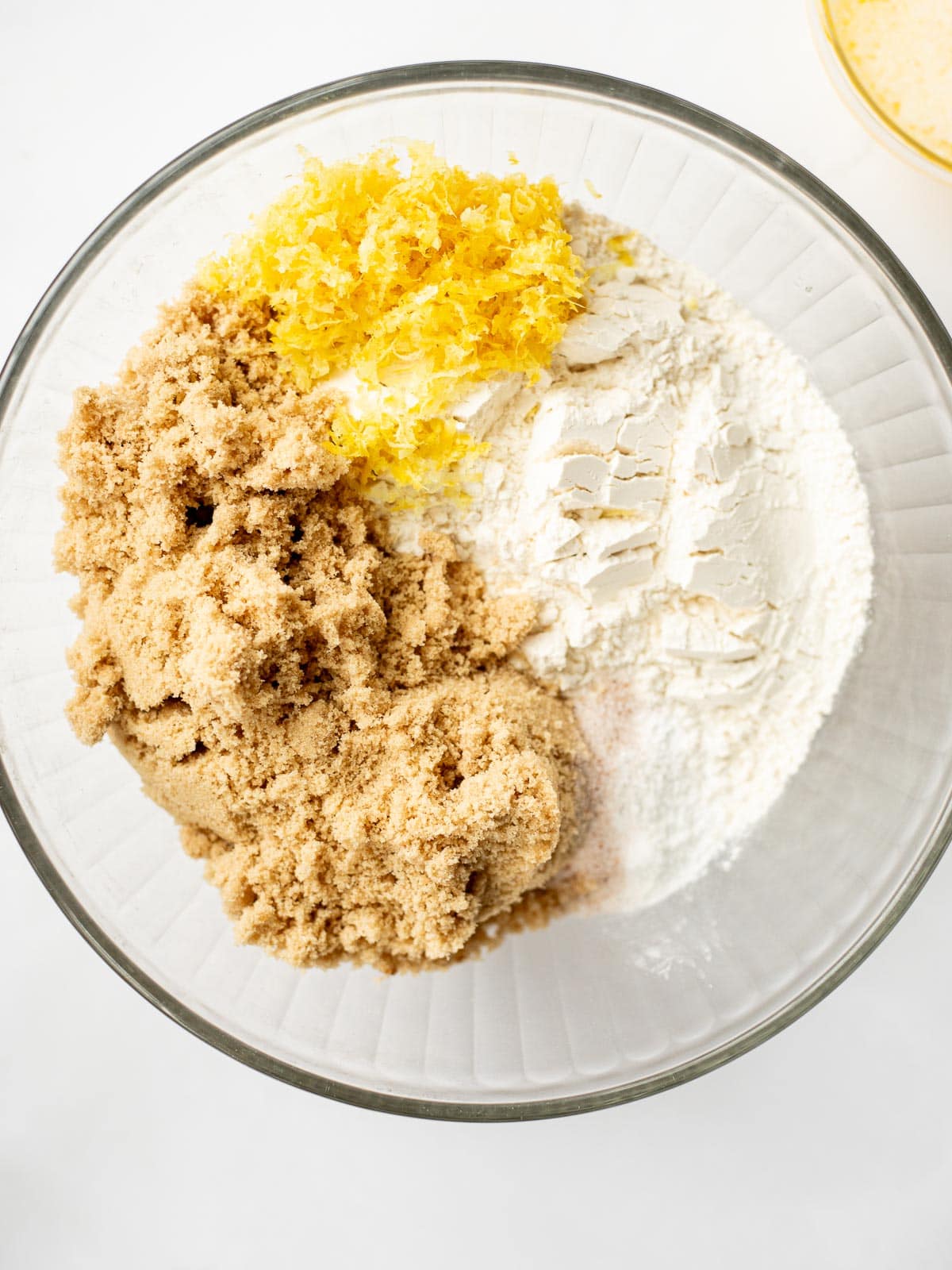 a glass bowl filled with flour, brown sugar, and lemon zest.