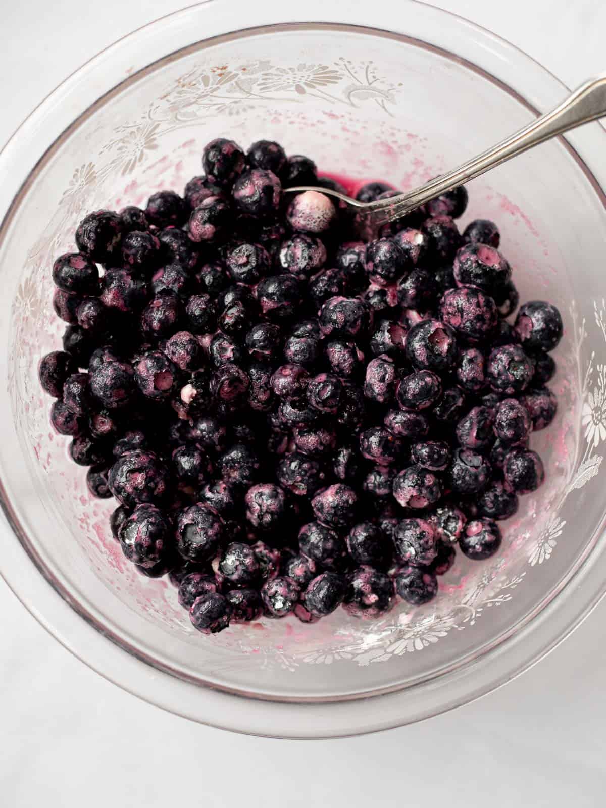 macerated blueberries in a glass bowl with a silver spoon.