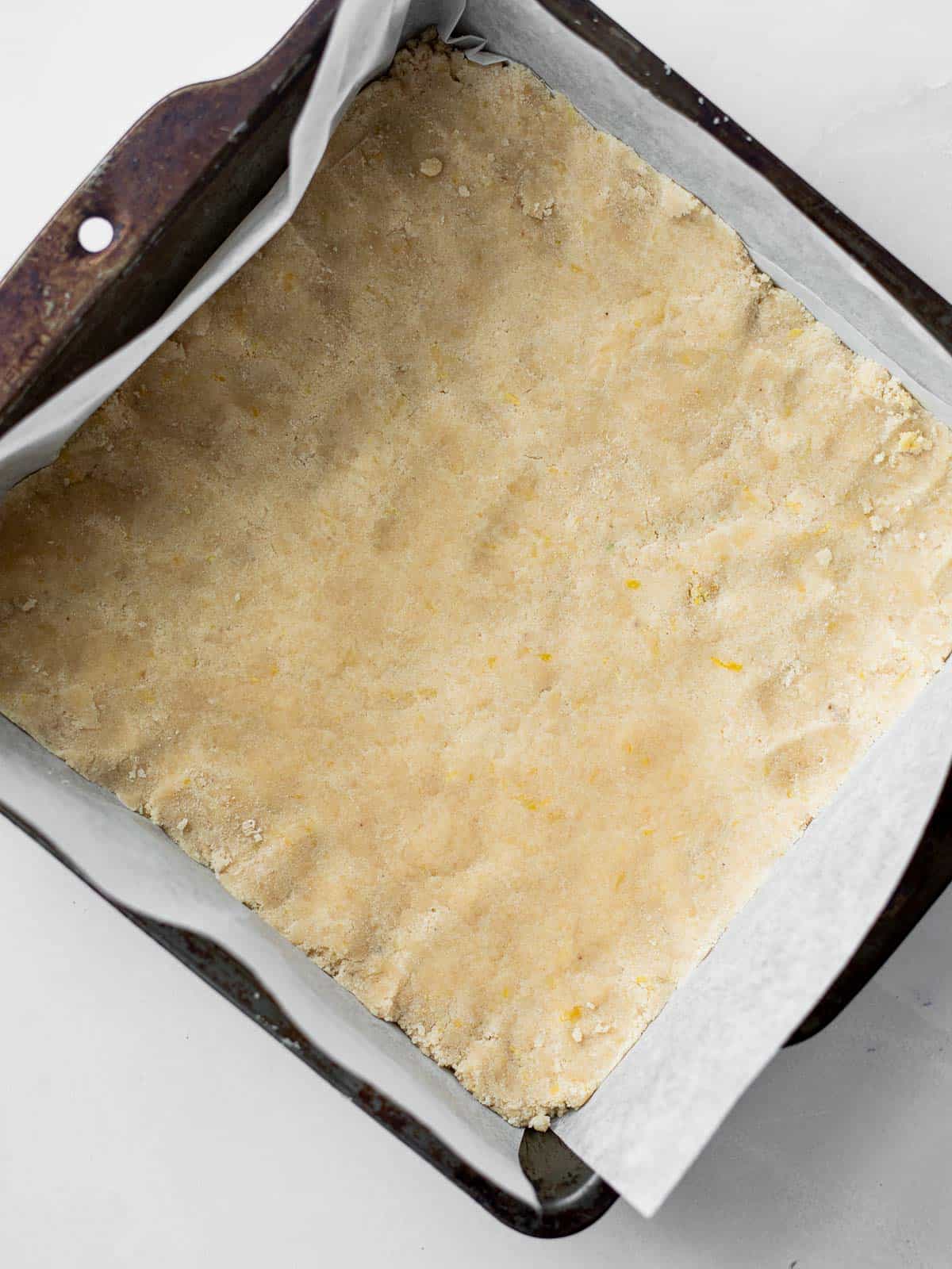 lemon shortbread dough pressed into a crust in a parchment lined baking pan.