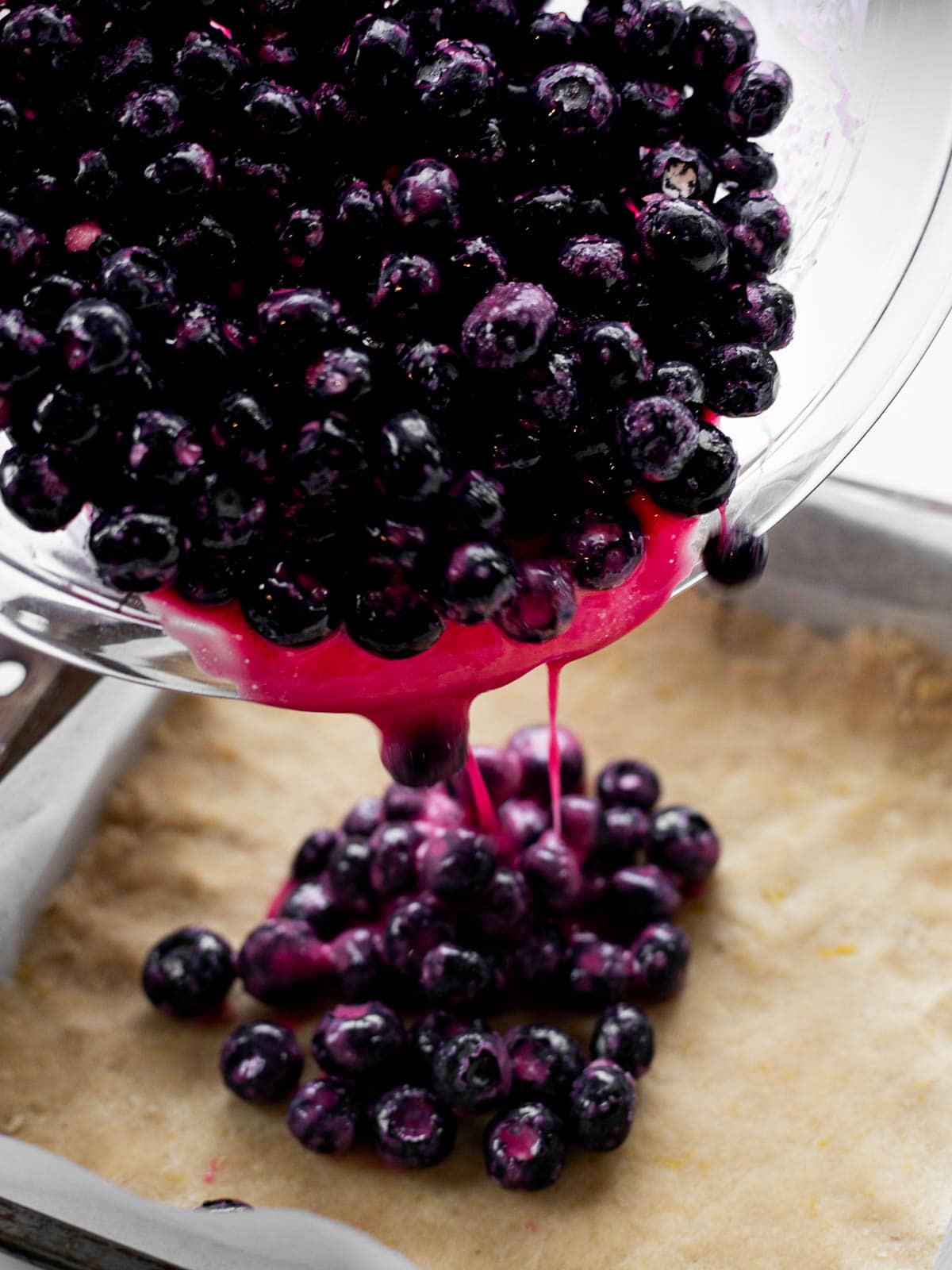 macerated blueberries pouring out of a bowl onto shortbread crust.