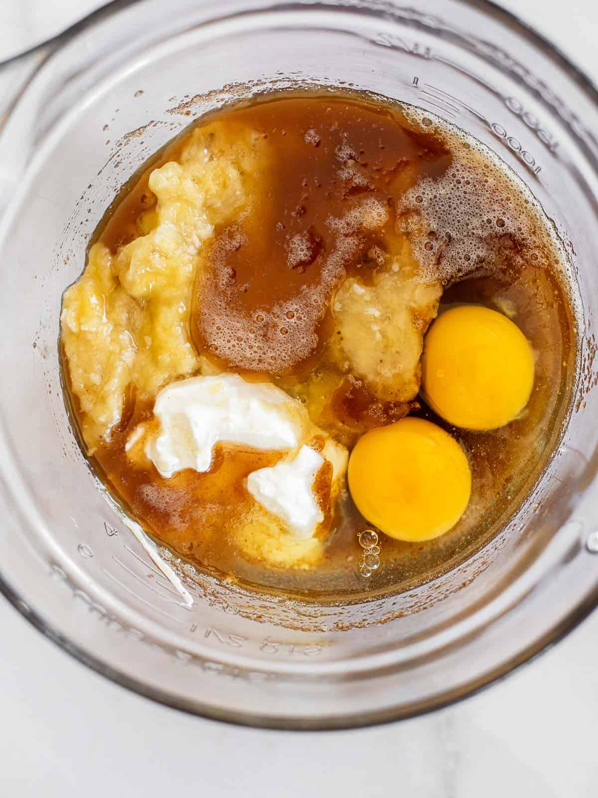 brown butter, sugar, eggs, bananas, and sour cream in a glass mixing bowl.